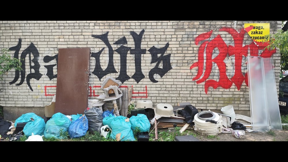 Śmieci piętrzące się pod murem z graffiti